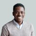 Smiling cheerful young adult african american ethnicity man looking at camera standing at home office background. Happy confident black guy posing for headshot face front close up portrait.